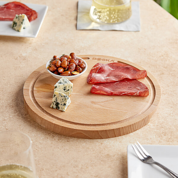 A Boska beech wood serving board with cheese, nuts, and meat on a table.