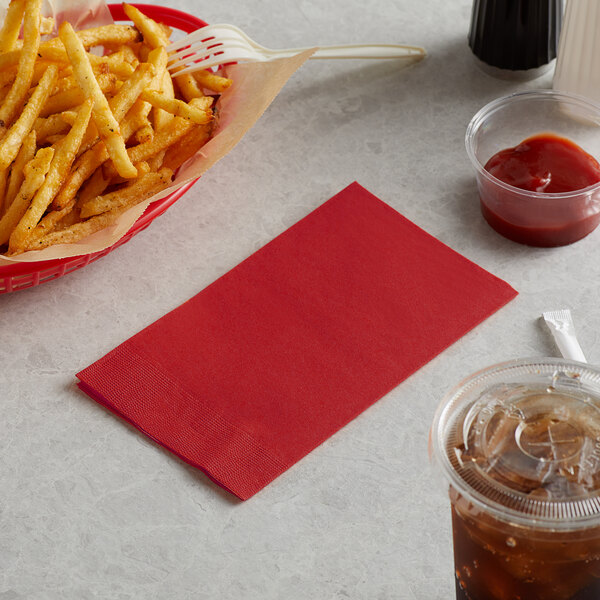 A basket of french fries and a red Choice 2-ply paper napkin on a table with a drink.