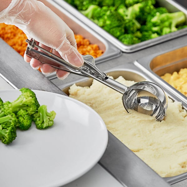 A person using a stainless steel round disher to scoop mashed potatoes.