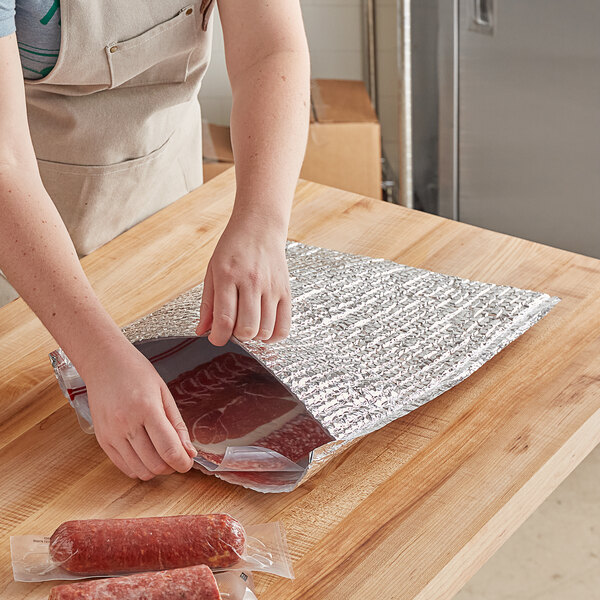 A person packing meat in a Lavex foil bubble mailer on a table.
