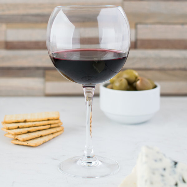 A Chef & Sommelier Cabernet wine glass filled with wine next to crackers and a bowl of olives.
