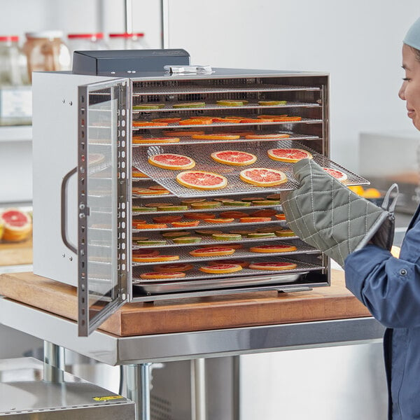 A woman using an Avantco stainless steel food dehydrator to dry fruit slices.