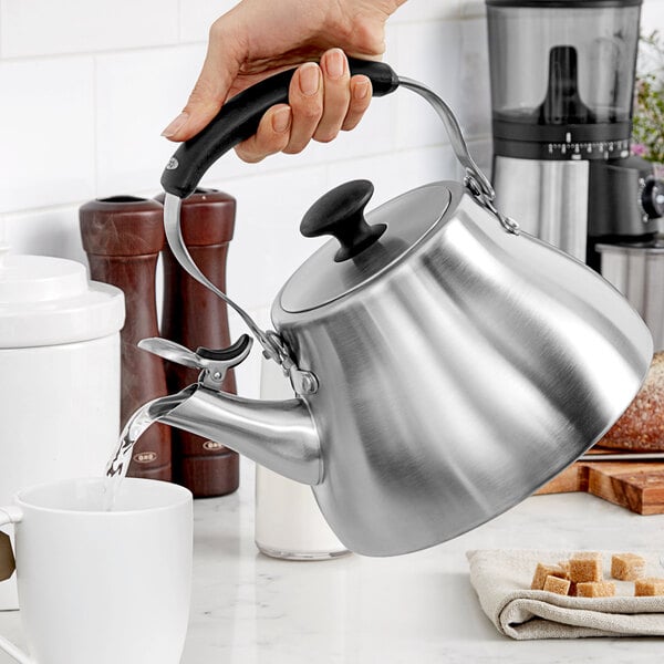 A person pouring water into a stainless steel OXO tea kettle.