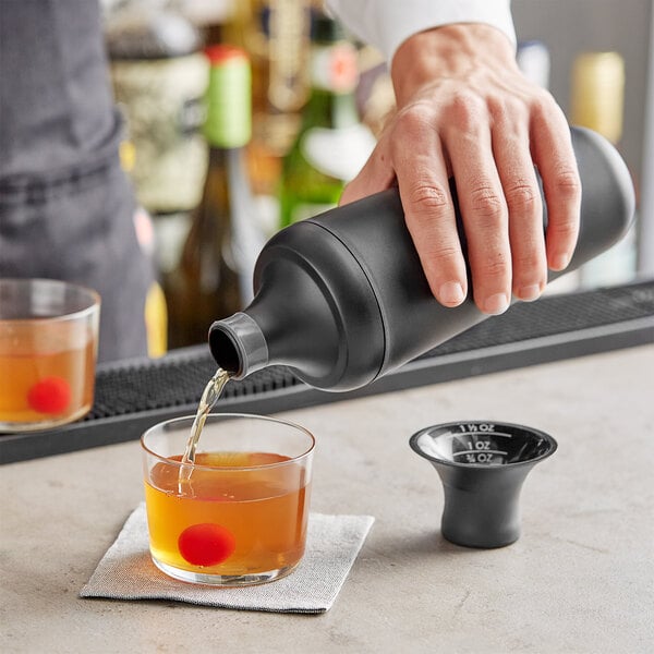 A person using an OXO plastic cocktail shaker to pour a drink into a glass.