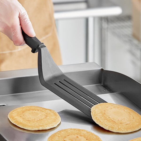 A person using a Fourté black slotted turner to flip pancakes.