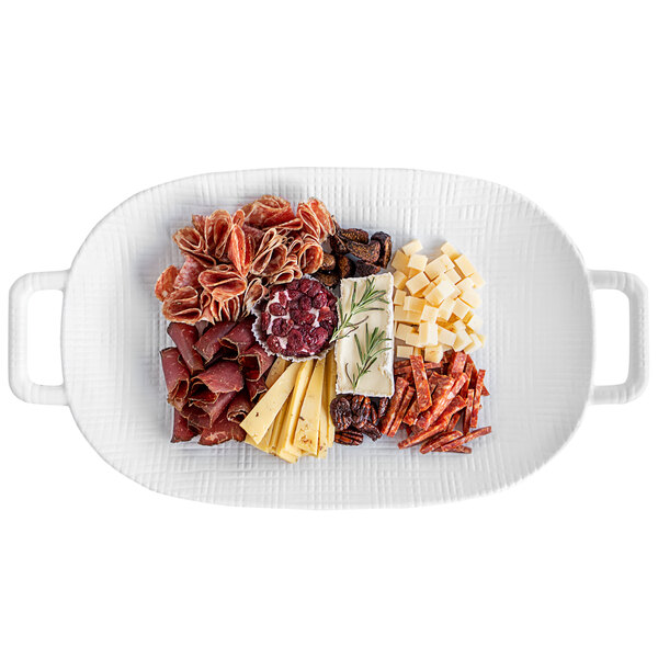 A Cal-Mil white melamine oval platter with meat and cheese on it.