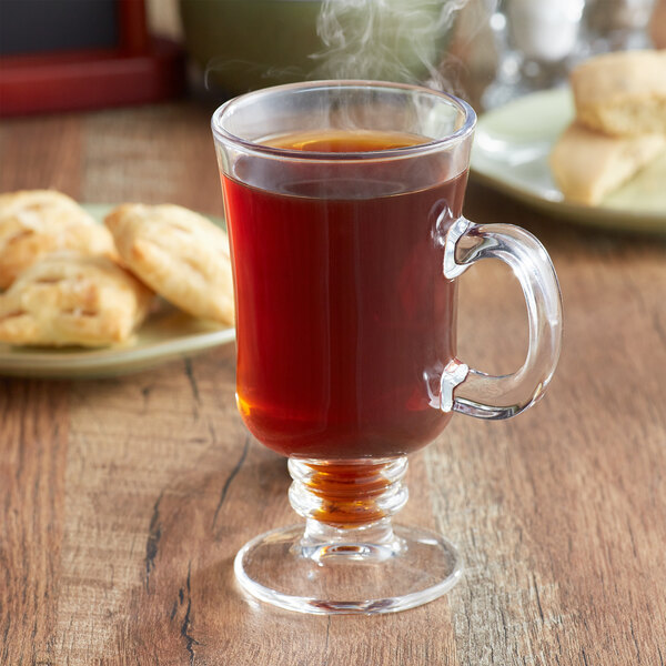 A glass mug filled with brown Ellis Mezzaroma Irish Cream coffee on a saucer with a pastry.