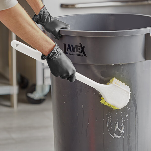 A person in gloves using a yellow Lavex pot scrub brush to clean a bucket.