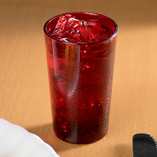 A Cambro ruby red plastic tumbler filled with red liquid and ice on a table.