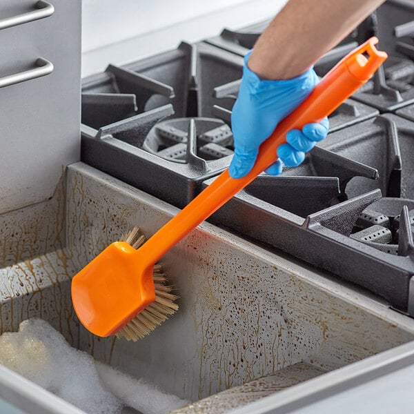A person in blue gloves cleaning a fryer with a Fryclone utility brush.