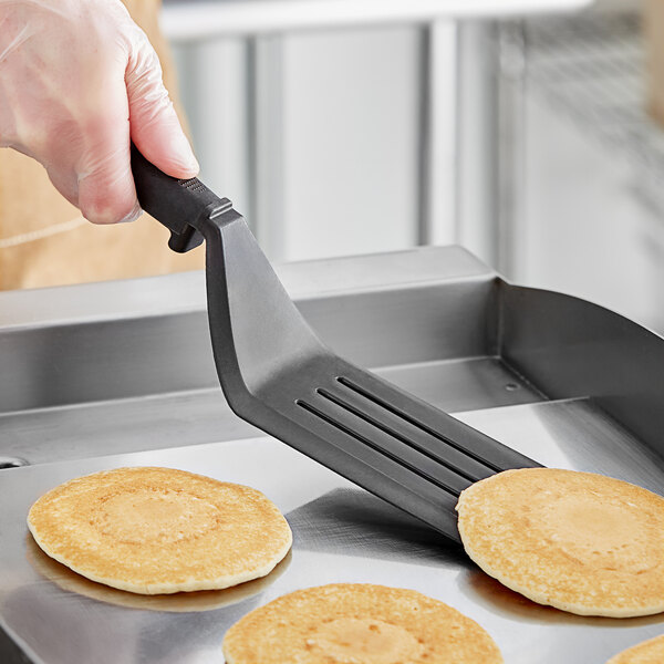A hand holding a Fourté black nylon slotted turner over pancakes.