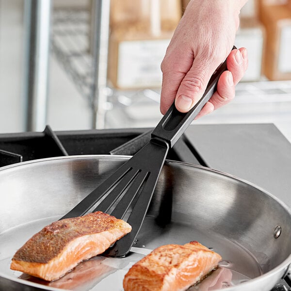 A person holding a black Fourt&#233; fish spatula over a pan of fish.