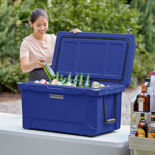 A woman putting a green bottle into a navy CaterGator outdoor cooler.