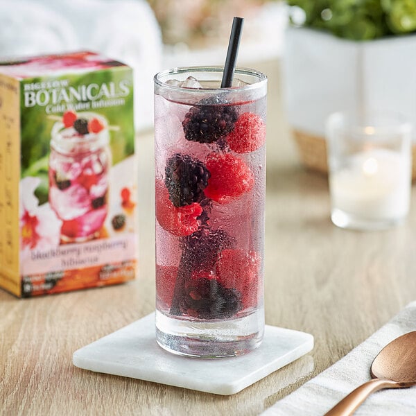 A glass of water with Bigelow Botanicals Blackberry Raspberry Hibiscus Cold Water Infusion and berries.