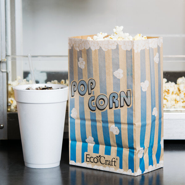 A Bagcraft Packaging EcoCraft popcorn bag with popcorn next to a cup of soda.