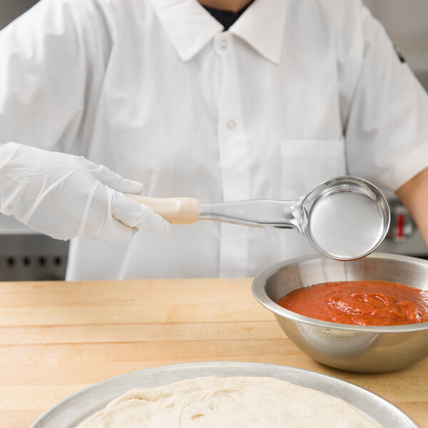 A person in a white shirt and gloves using a Vollrath ivory spoodle to serve red sauce from a bowl.