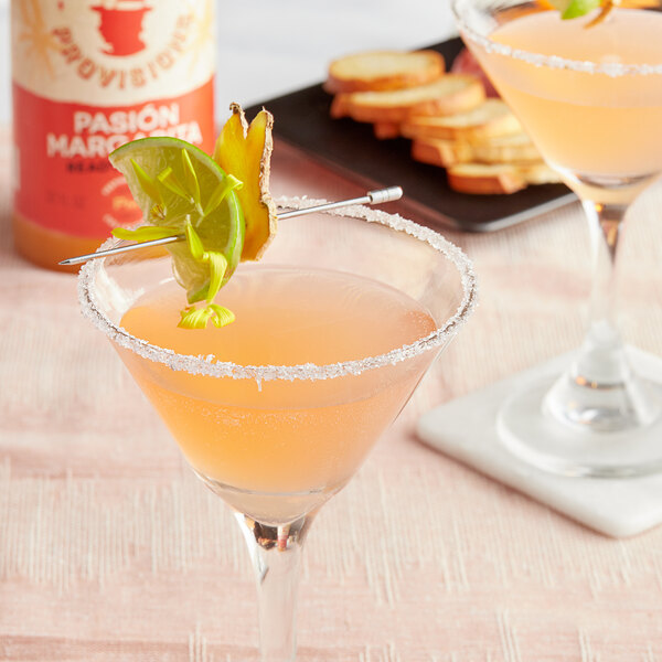 A glass of pink Top Hat Provisions Passion Fruit Margarita mix with a lime slice on the rim.