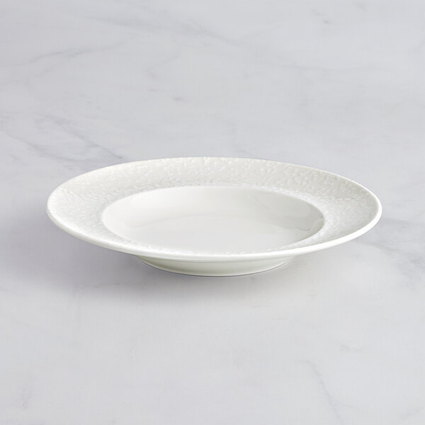 A white porcelain plate with an embossed rim on a marble surface.