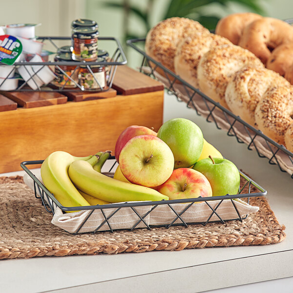 A Gunmetal gray rectangular wire basket filled with fruit and bread, including a banana and a green apple.
