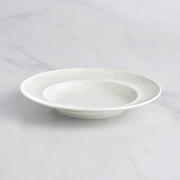 A RAK Porcelain ivory deep plate with an embossed rim on a marble surface.