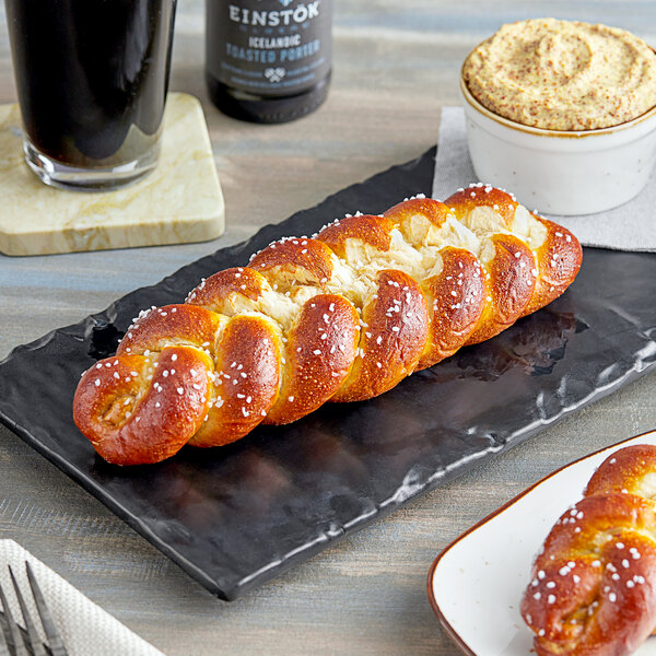 A plate of Dutch Country Foods soft pretzel braids on a table near a glass of dark liquid.