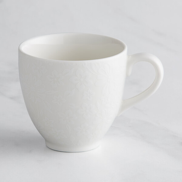 A white RAK Porcelain cup with an ivory floral design and handle.