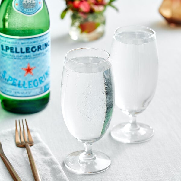 A glass of water next to a San Pellegrino Sparkling Natural Mineral Water bottle.