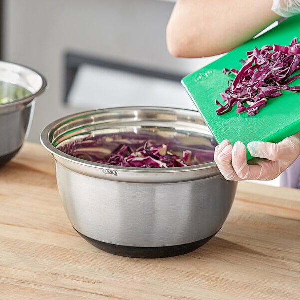 A person in gloves putting shredded red cabbage into a Choice stainless steel mixing bowl with a silicone bottom.
