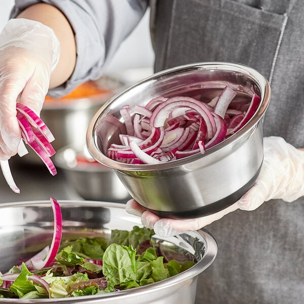 A person in gloves holding a Choice stainless steel mixing bowl with a red and white salad.