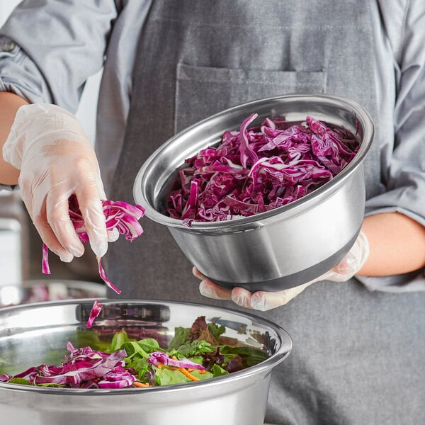 A woman in a chef's uniform holding a bowl of shredded red cabbage in a Choice stainless steel mixing bowl with a silicone bottom.