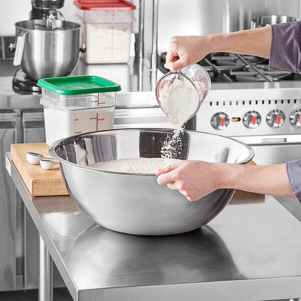 A woman pouring flour into a Choice stainless steel mixing bowl.