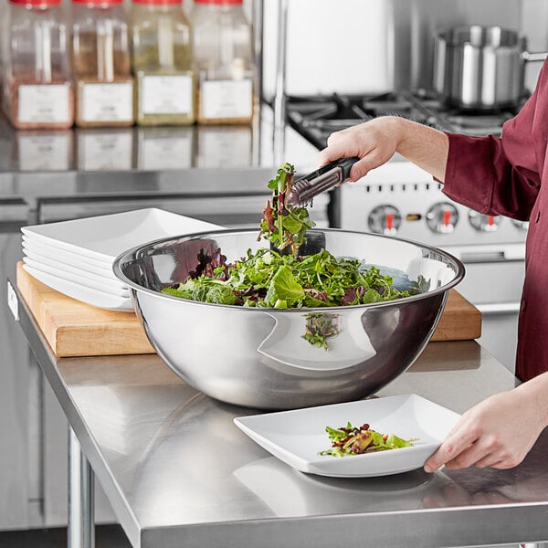 A woman pouring salad greens into a Choice stainless steel mixing bowl on a kitchen counter.