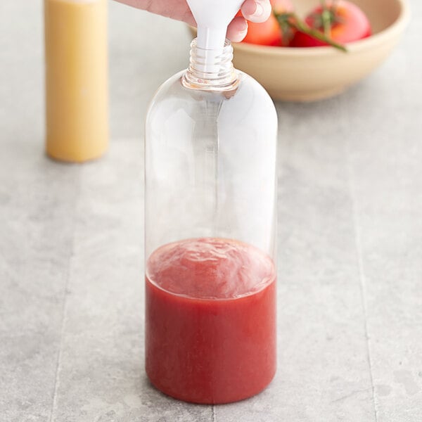 A hand pouring red tomato sauce into a 32 oz. Boston Round PET clear bottle.