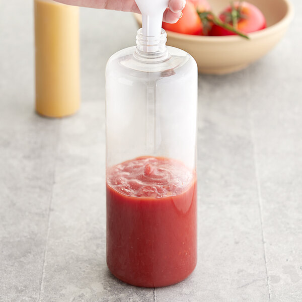 A hand pouring red tomato sauce into a clear plastic bottle.