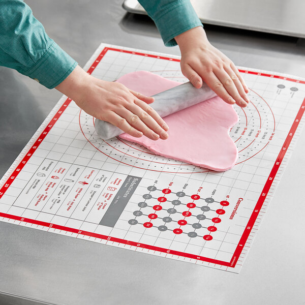 A person using an OXO Good Grips silicone pastry mat to roll out pink dough.