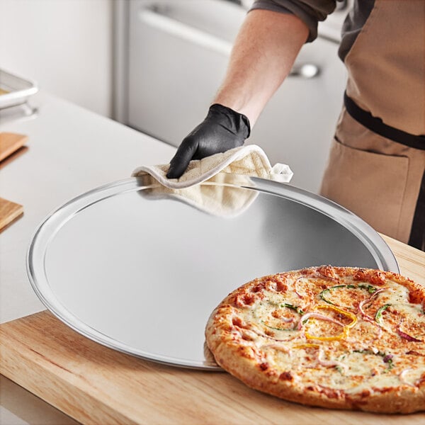 A person holding a pizza on a Choice aluminum pizza pan.