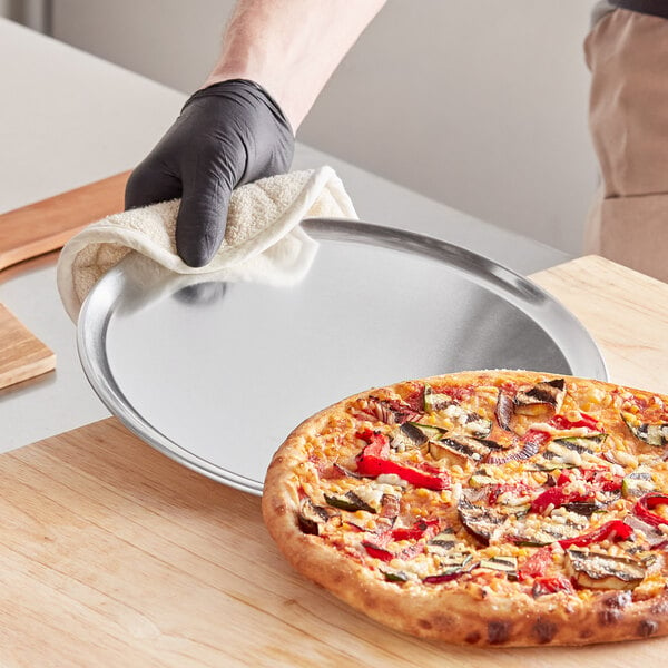 A hand in a black glove holding a pizza on a Choice aluminum coupe pizza pan.