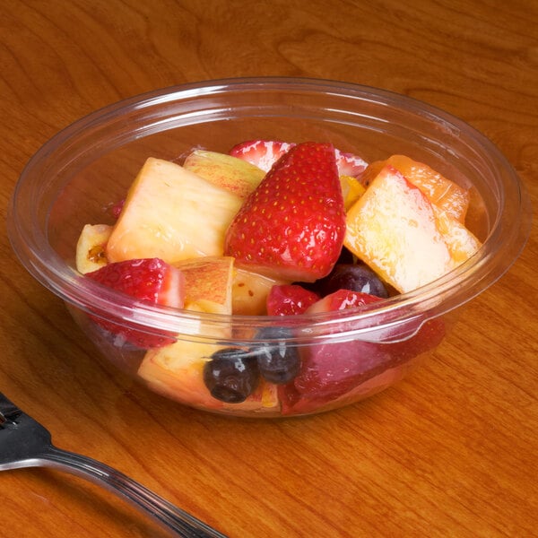 A clear Sabert round bowl filled with fruit salad on a table.