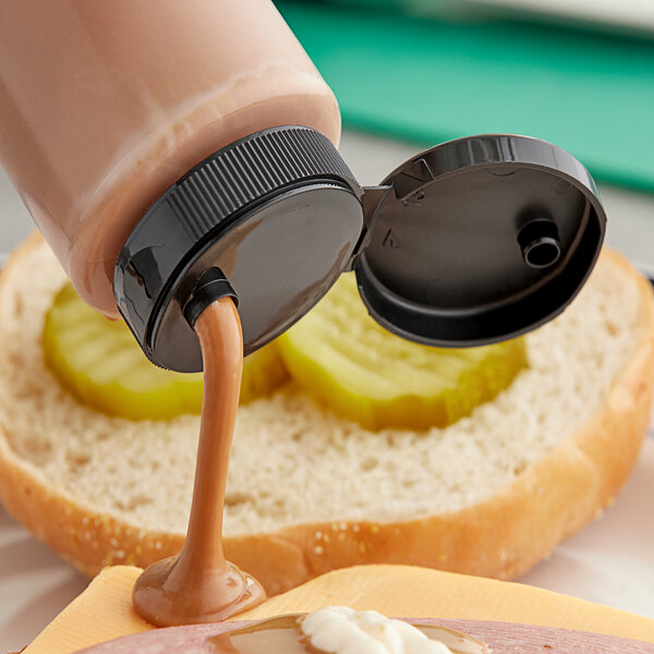 A 38/400 black dispensing cap pouring brown sauce onto a sandwich.