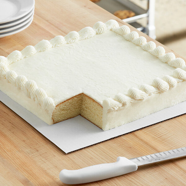 A square white frosted cake on a white corrugated board.