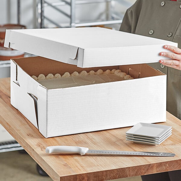 A person holding a white corrugated bakery box with a cake inside.