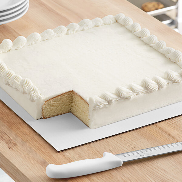 A white cake on a white corrugated square cake board with a slice missing.