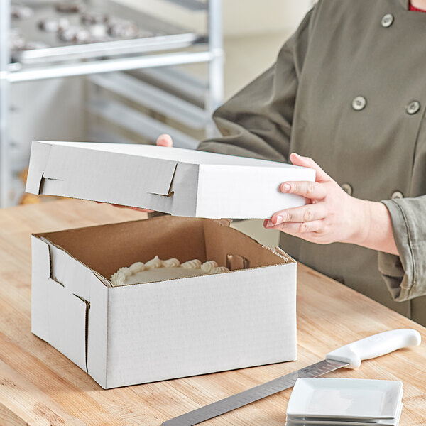 A person opening a white bakery box with a white cake inside.