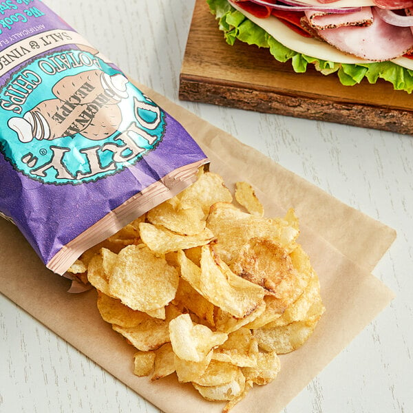 A bag of Dirty Salt and Vinegar Potato Chips on a table next to a sandwich.
