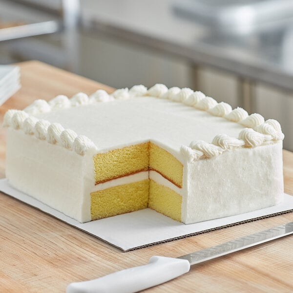 A white sheet cake with a slice cut out on a white corrugated cake pad.