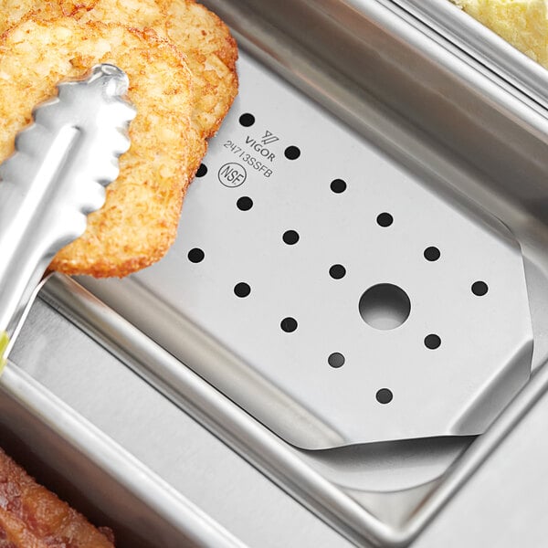 A Vigor stainless steel hotel pan false bottom on a counter with food tongs.