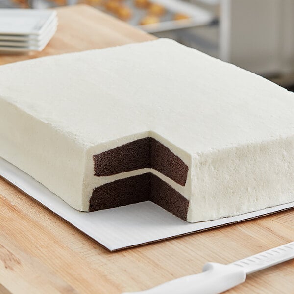A white double-layer cake cut in half on a white Double-Wall Corrugated Half Sheet Cake Pad.