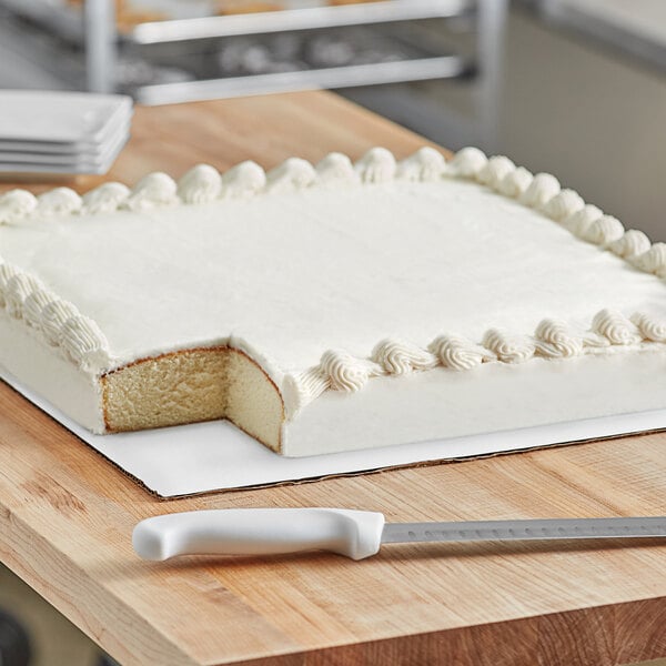 A frosted cake on a white square cake board with a knife.