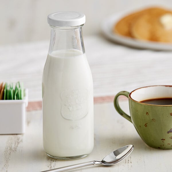 An Acopa glass milk bottle next to a cup of coffee.