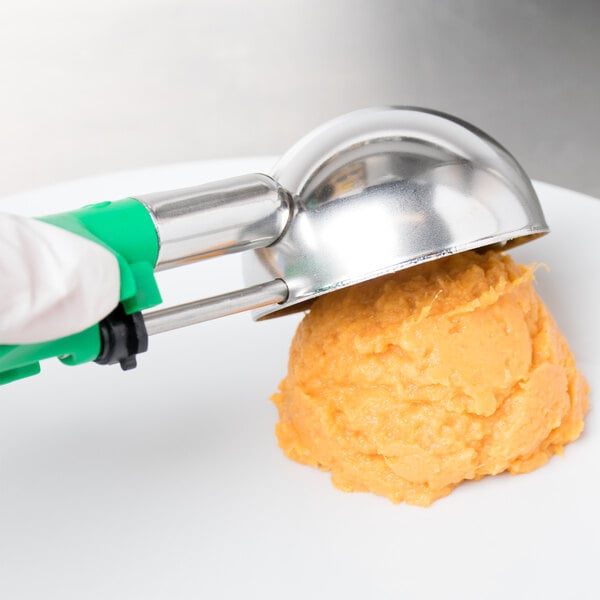 A person using a Vollrath green-handled metal scoop to serve food.